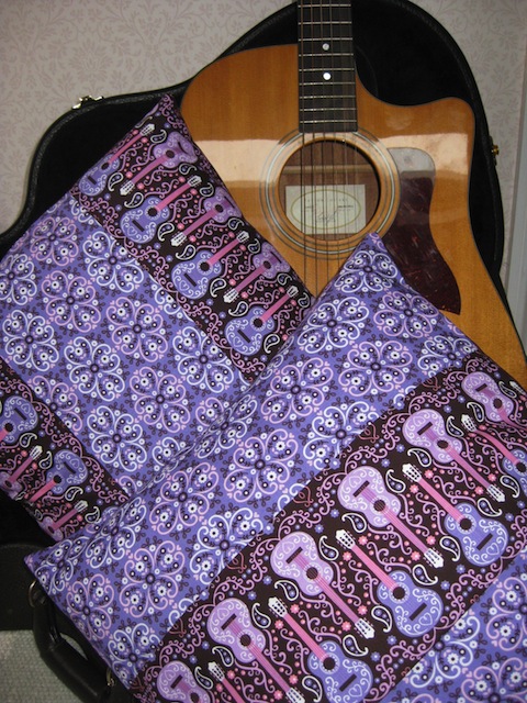 Retro-style handmade cushions with guitars in lavender and pink on a dark background.