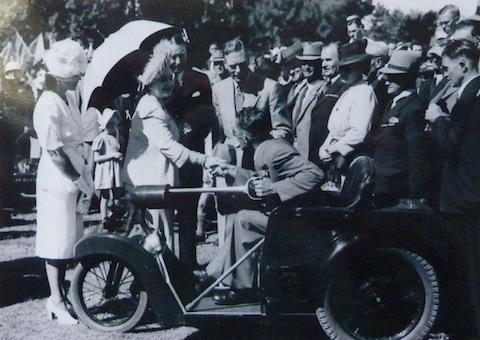 King George VI and Queen Elizabeth (later the Queen Mother) pictured with a Nelco Solocar. Who is the person in the driving seat?