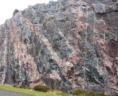 The exposed rock face I believe showing Lewisian Gneiss a metamorphic rock. the irregular colour banding might be caused by mixing while still in a molten state. Can any geologist reader confirm or explain?