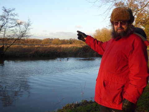 Jim Allen on the towpath of the Wey Navigation pointing across the thw water meadows and flood plain.