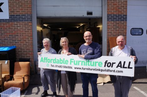Outside the FurnitureLink warehouse, volunteers, John and Sue with Wendy and Kenny Watson in the middle holding the FurnitureLink board.